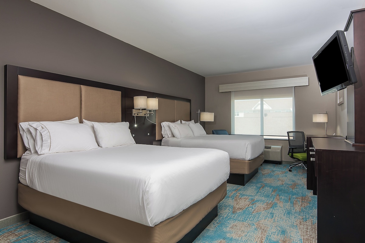 Habitación de hotel con dos camas, un escritorio, una silla y un televisor.