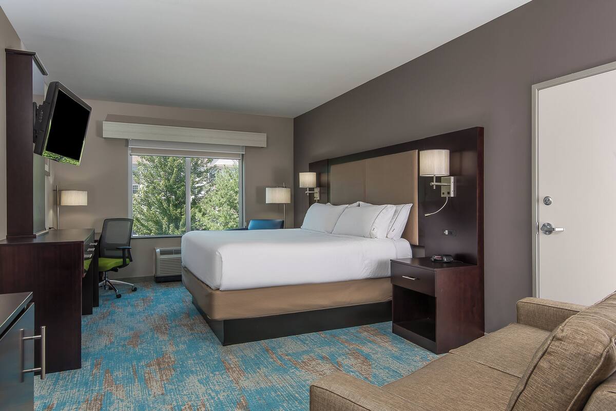 A hotel room with a bed, desk, chair, TV, and a window with a view.