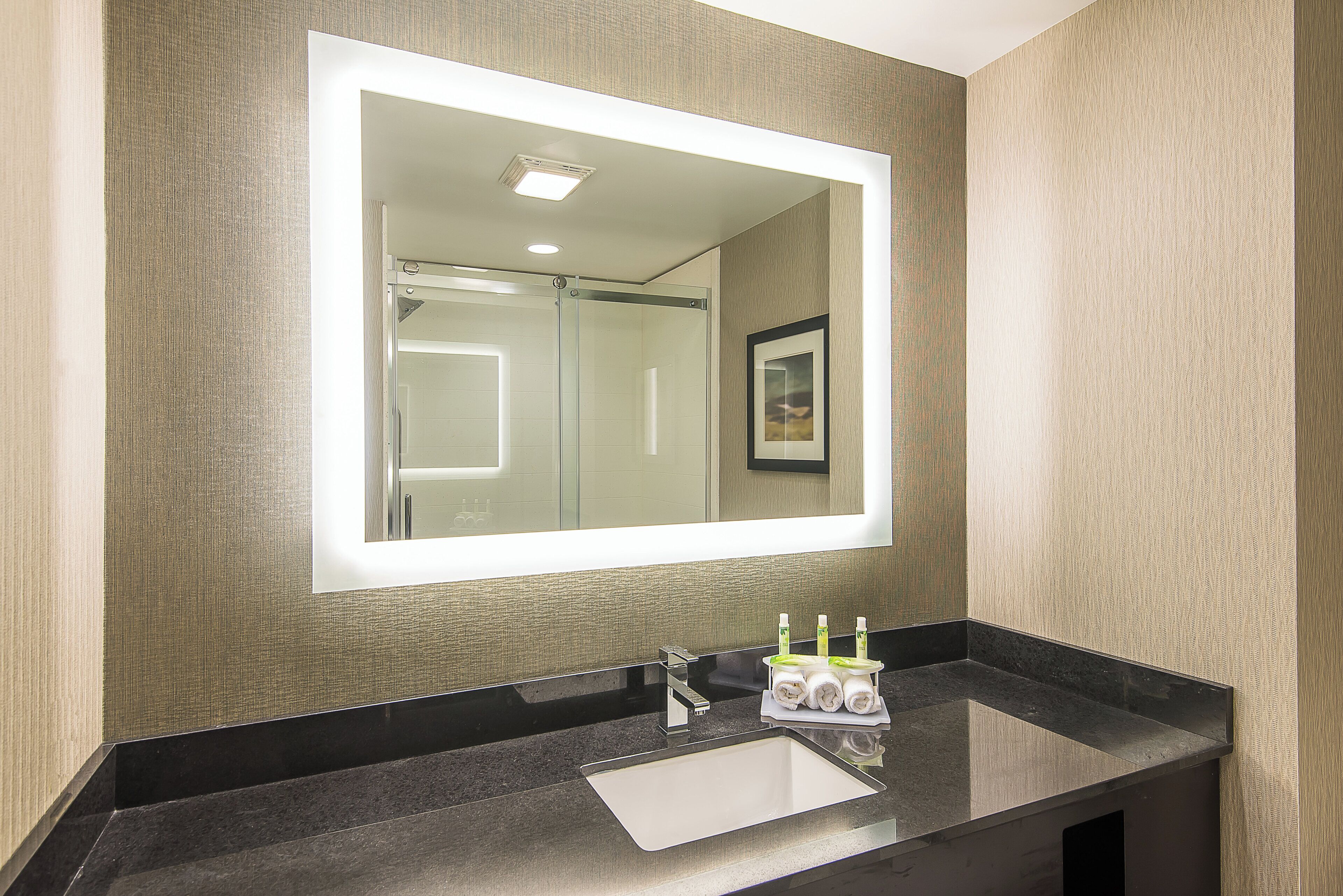 Un baño con un espejo grande, un lavabo y un perchero para toallas.
