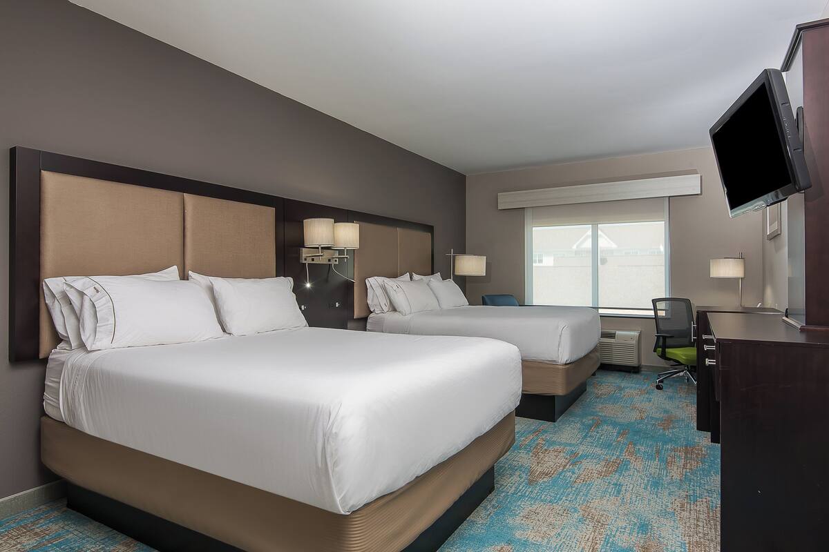 A hotel room with two beds, a desk, a chair, and a TV.