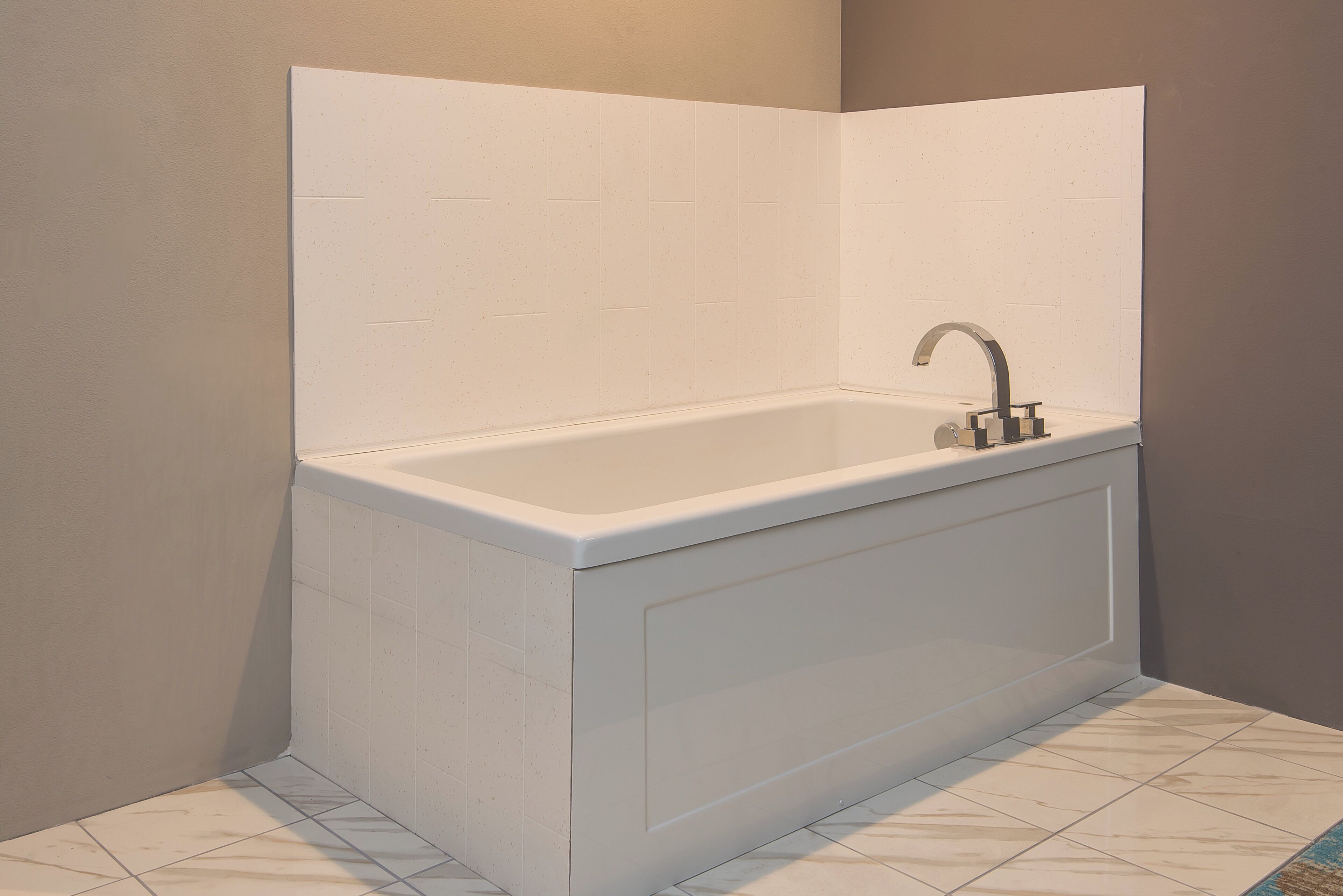A corner bathroom with a white bathtub, a modern faucet, and a tiled floor.