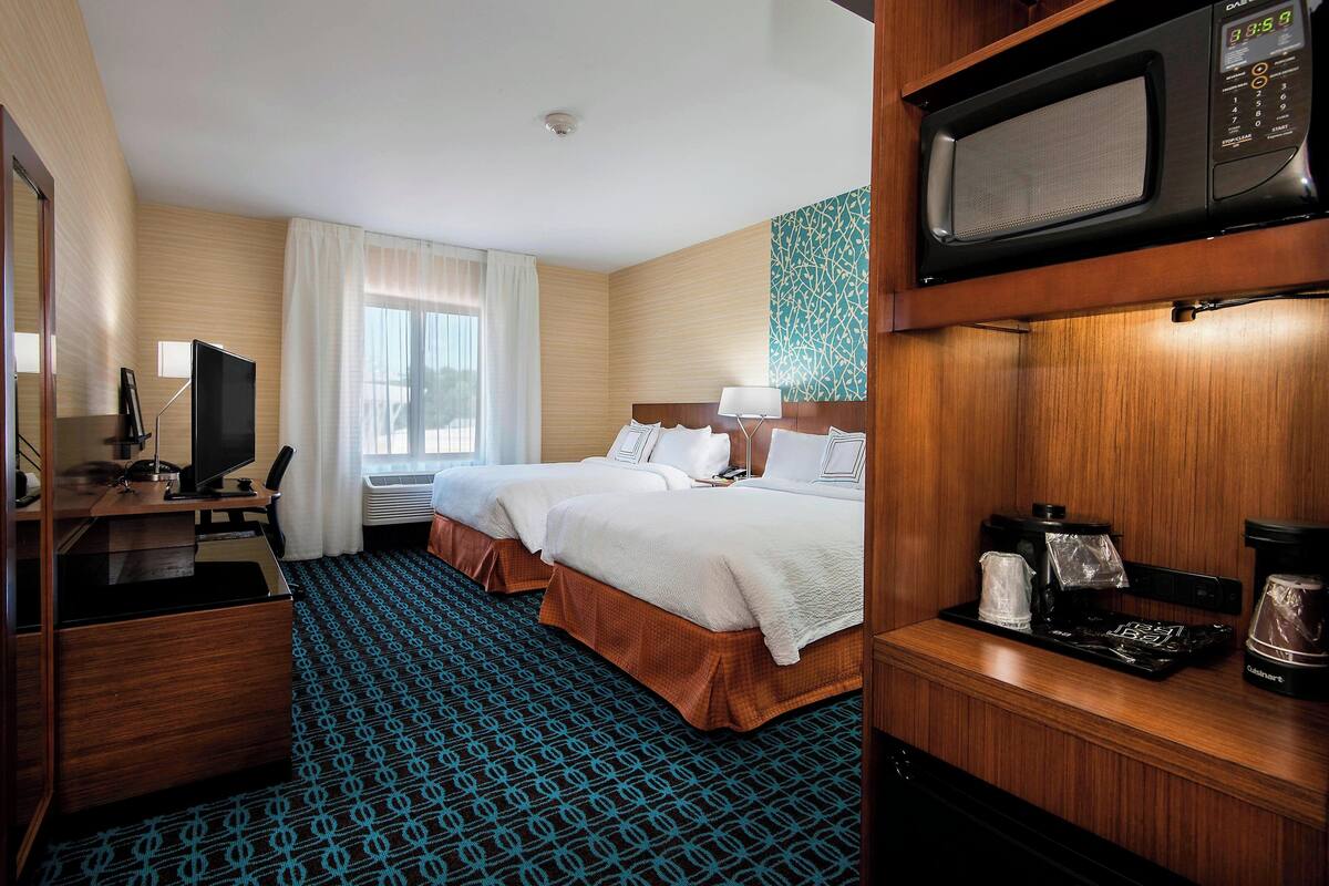 A hotel room with two beds, a desk with a computer, a TV, a microwave, and a coffee maker.
