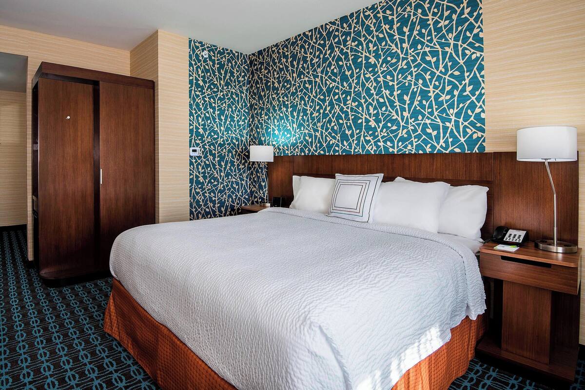 A hotel room with a large bed, wooden wardrobe, patterned wallpaper, and bedside lamps.