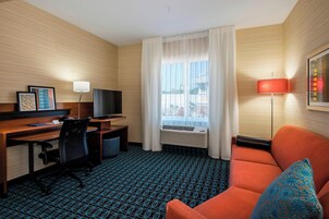 Habitación de hotel con pared de madera, un escritorio con computadora y televisor, un sofá y una ventana con cortinas.