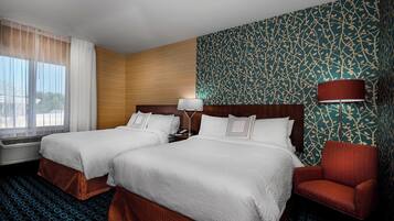 Habitación de hotel con dos camas, un sillón rojo, un papel tapiz estampado y una ventana con cortinas.