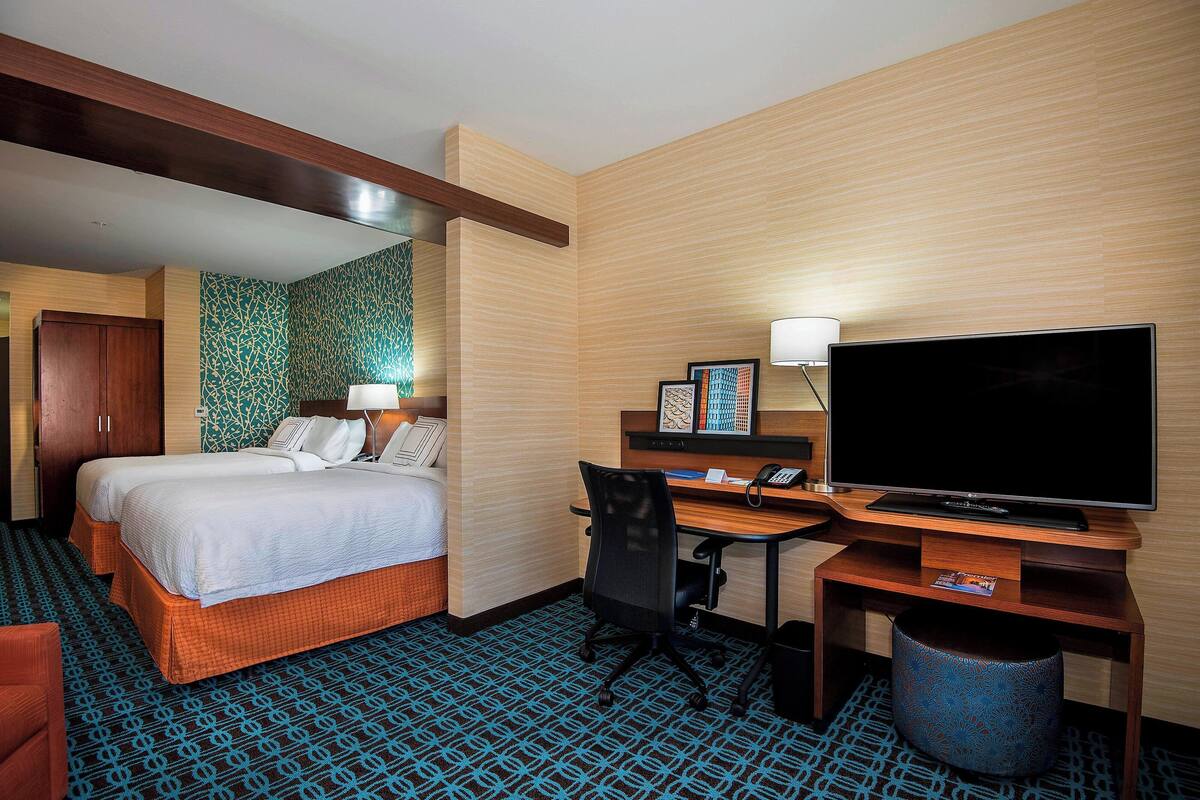 A hotel room with a bed, desk, chair, TV, and a patterned carpet.