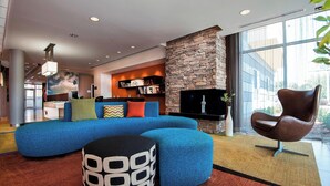 A modern living room with a blue sectional sofa, a stone accent wall, a flat-screen TV, and a comfortable armchair. - Fairfield Inn & Suites Little Rock Benton (Benton)