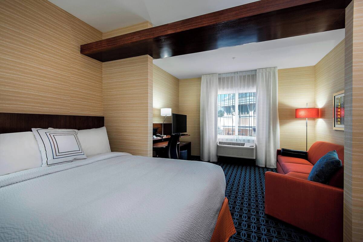 A hotel room with a large bed, a desk, a chair, and a window with curtains.