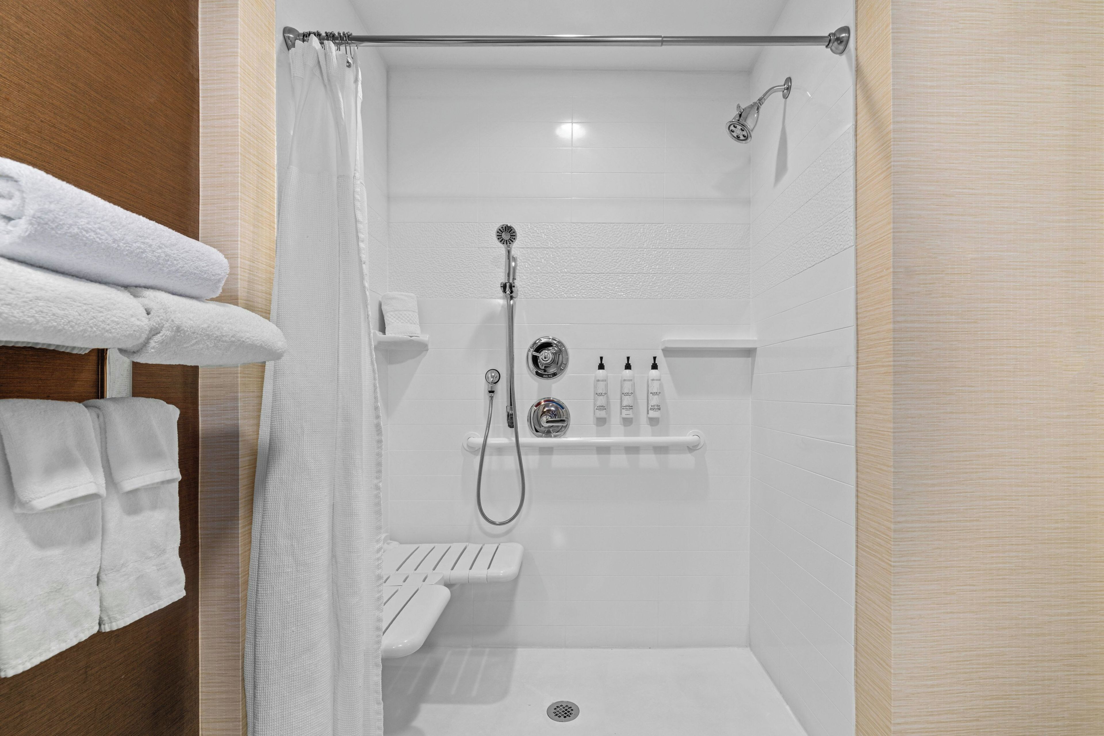 Área de duche moderna com porta de vidro, chuveiro manual e um conjunto de produtos de higiene num armário.