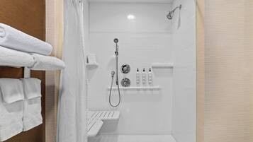 Área de duche moderna com porta de vidro, chuveiro manual e um conjunto de produtos de higiene num armário.