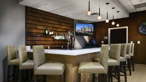 A bar area with a wooden wall, multiple bar stools, a TV screen, and a ceiling with pendant lights. - Fairfield Inn & Suites Little Rock Benton (Benton)