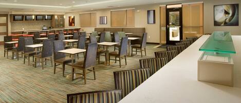 A hotel dining area with multiple tables and chairs, a reception desk, and a large window.