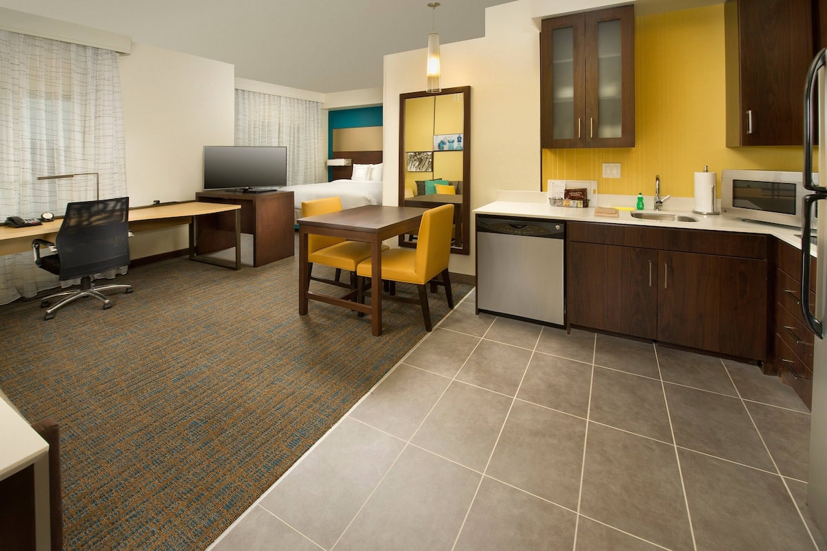 A hotel room with a bed, desk, chair, television, and a kitchenette.