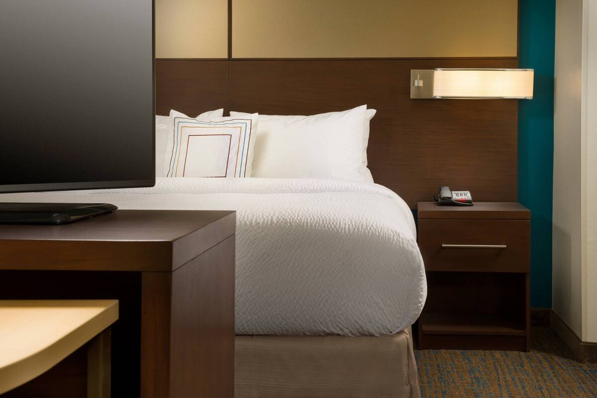 A neatly arranged hotel room with a large bed, a bedside table, a TV, and a nightstand with a lamp.