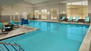 Une piscine intérieure à l’eau d’un bleu cristallin, entourée de chaises longues et bordée d’une terrasse carrelée.