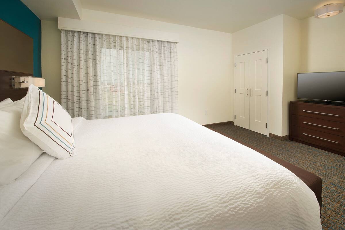 A hotel room with a large bed, a television on a dresser, and a wardrobe.