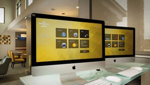 Deux ordinateurs Apple iMac sont posés sur un bureau en verre, accompagnés d’un clavier et d’une souris. L’écran affiche une interface de gestion hôtelière.
