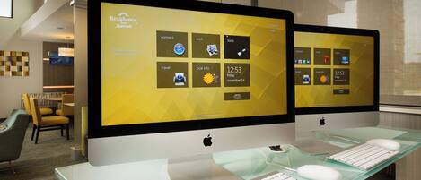 Two Apple iMac computers on a glass desk with a keyboard and mouse, displaying a hotel management interface.