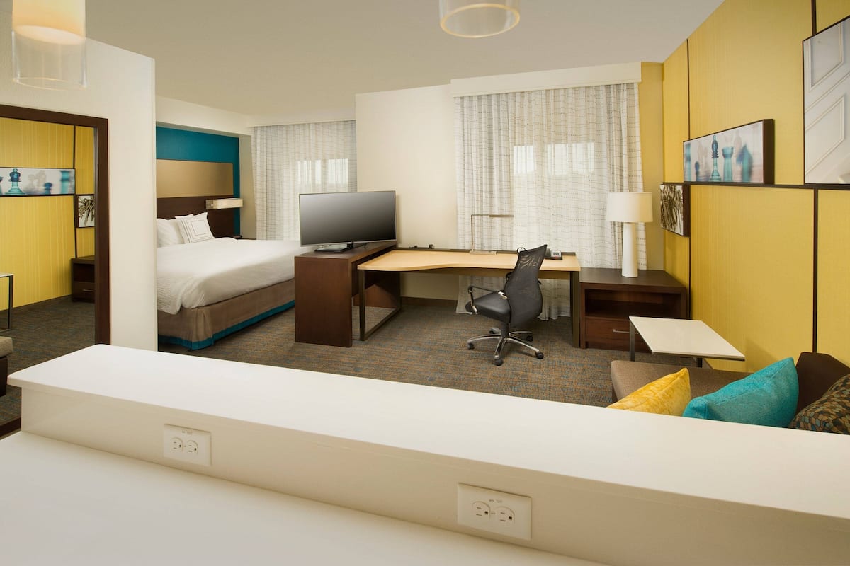 A hotel room with a bed, desk, chair, television, and a large window with curtains.