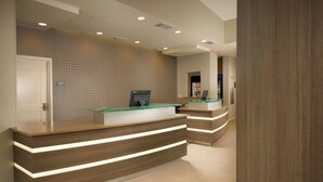 Un comptoir d’accueil moderne doté d’un plateau en verre et d’un socle en bois, d’un écran numérique et d’une enseigne indiquant qu’il s’agit d’un hôtel.