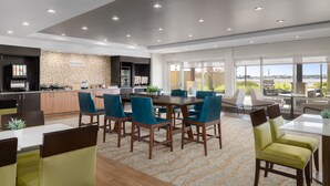 Un moderno vestíbulo de hotel con zona de comedor, cocina y grandes ventanales que ofrecen vistas.