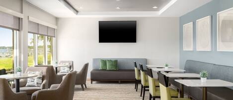 A modern dining area with a flat-screen TV mounted on the wall, a sofa, and several tables and chairs.