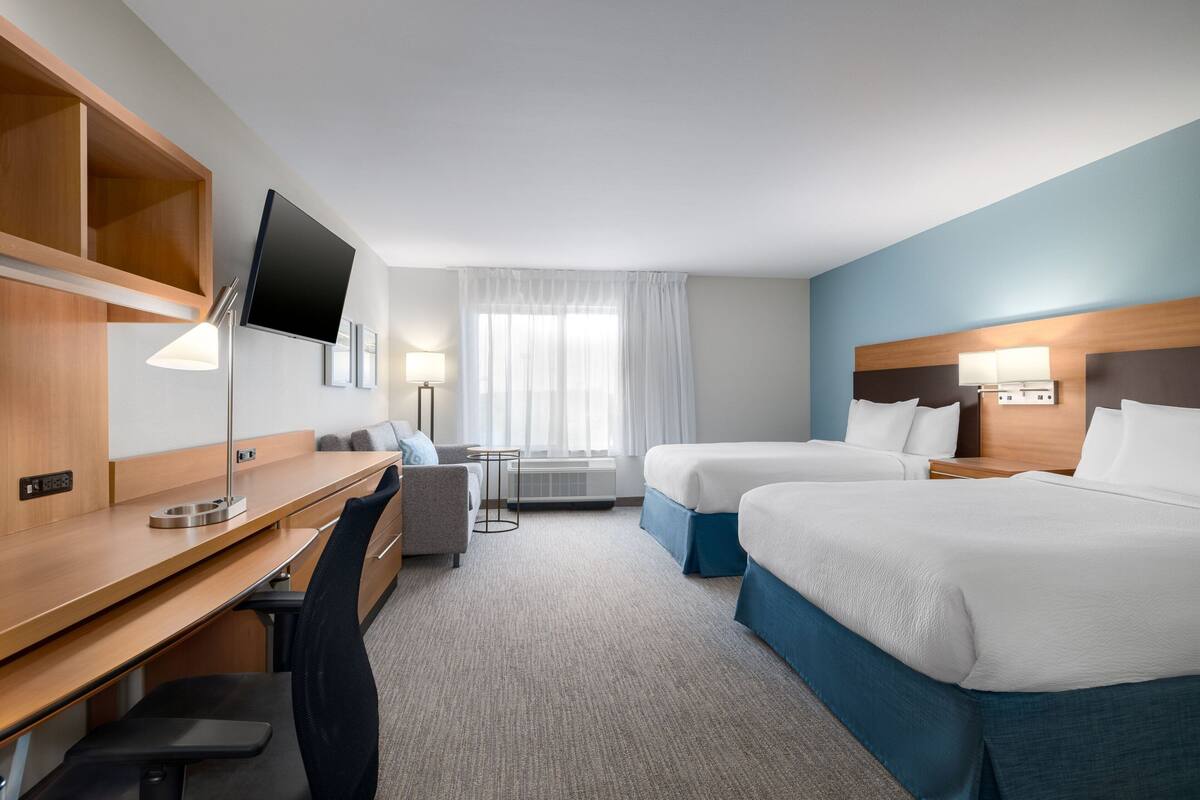 Hotellihuone, jossa on kaksi sänkyä, työpöytä, tuoli, televisio ja ikkuna, jossa on verhot.