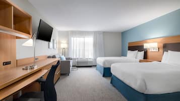 Quarto de hotel com duas camas, uma escrivaninha, uma cadeira, televisão e janela com cortinas.