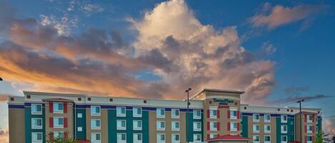 A hotel with a parking lot, multiple floors, and a large cloud in the sky.
