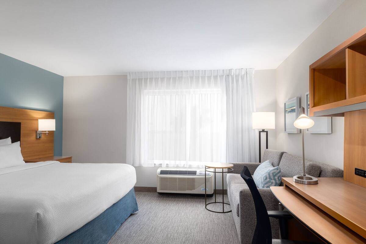 Hotellihuone, jossa on sänky, työpöytä, tuoli, pieni pöytä ja ikkuna, jossa on verhot.