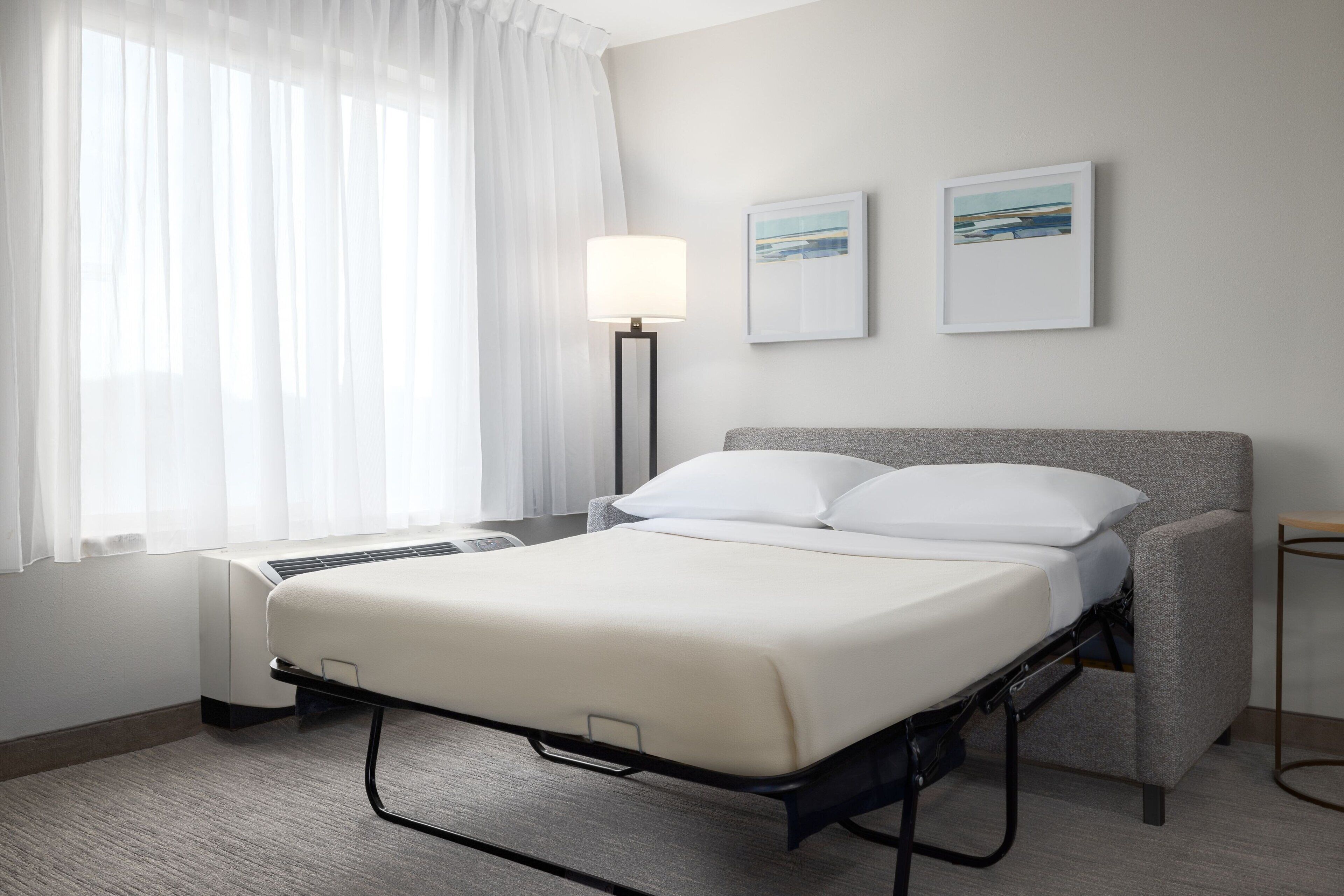 A hotel room with a bed, a bedside table, a lamp, and two framed pictures on the wall.