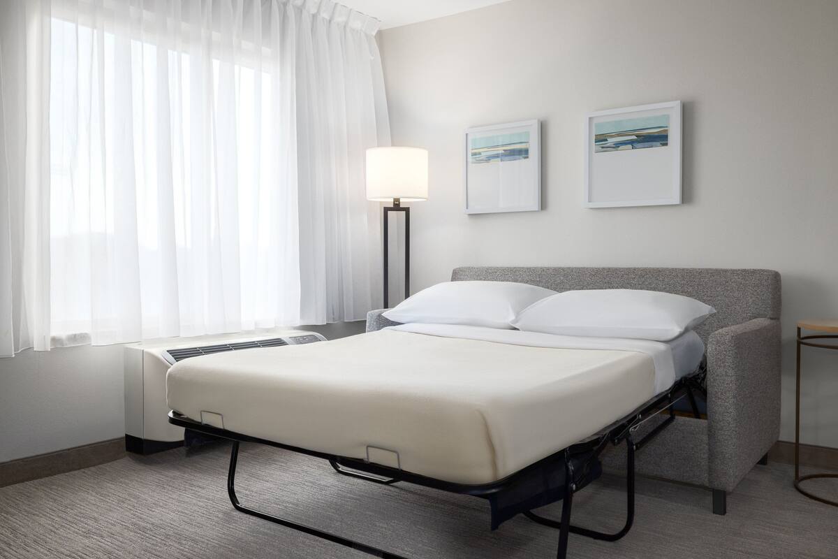 Una habitación de hotel con una cama, una mesita de noche, una lámpara y dos cuadros en la pared.