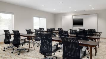 Une salle de conférence équipée de plusieurs tables et chaises, de grandes fenêtres et d’un téléviseur fixé au mur.