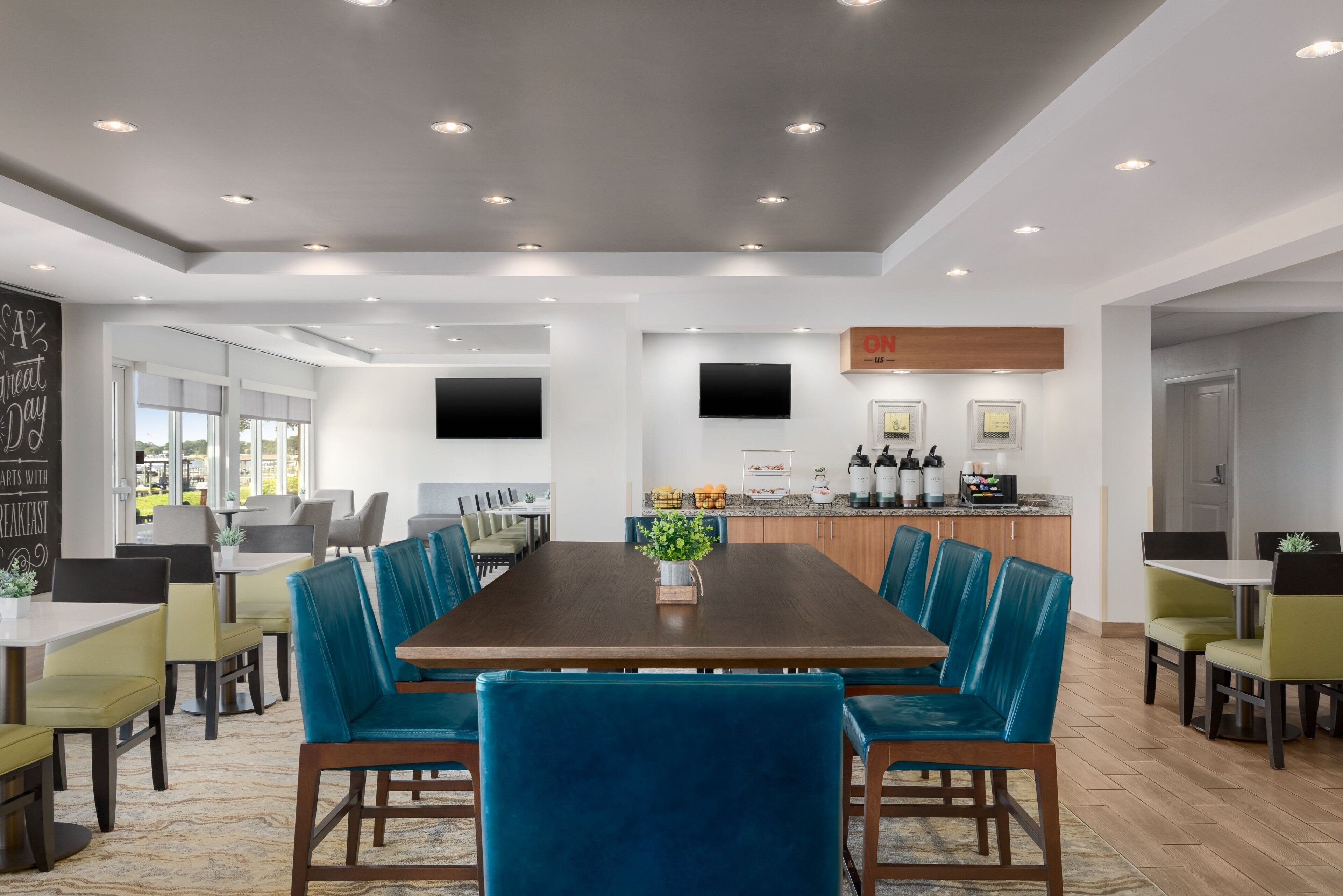 Un espace repas moderne avec une longue table, des chaises à revêtement bleu et une plante placée au centre.