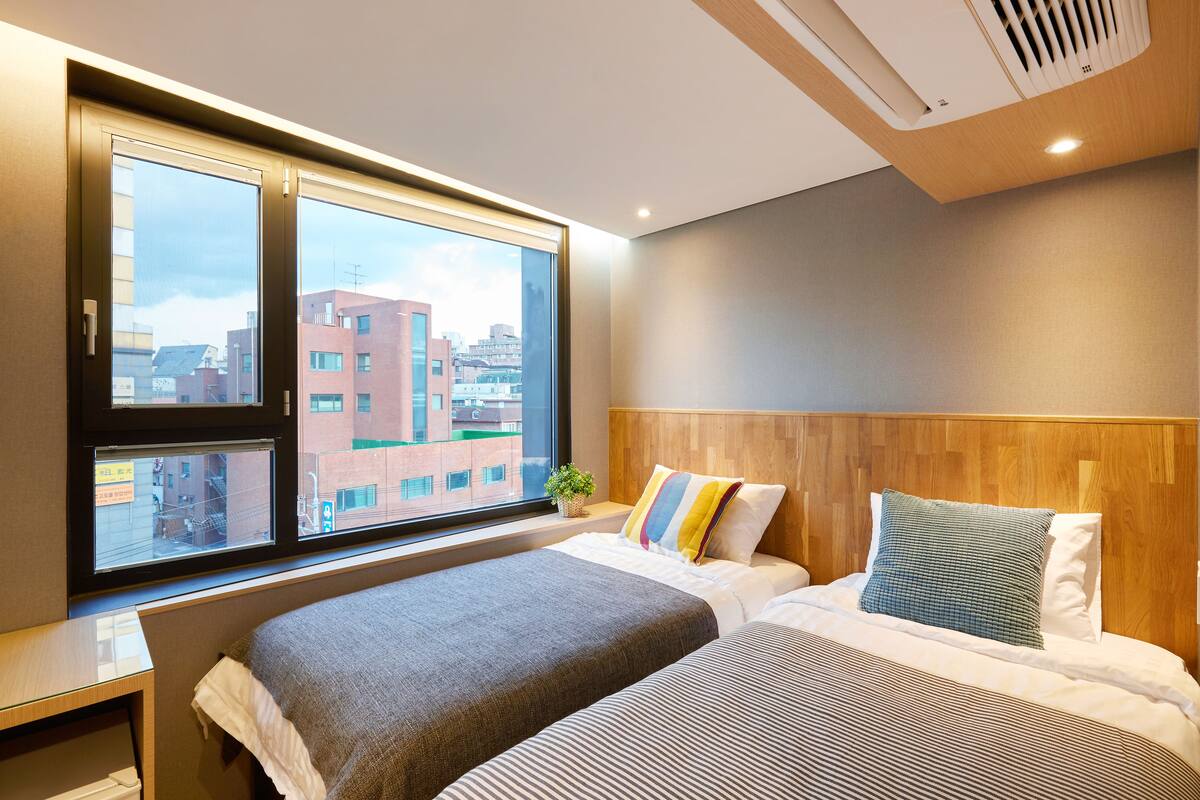 A modern hotel room with a large window, a wooden headboard, and a bed with striped bedding.