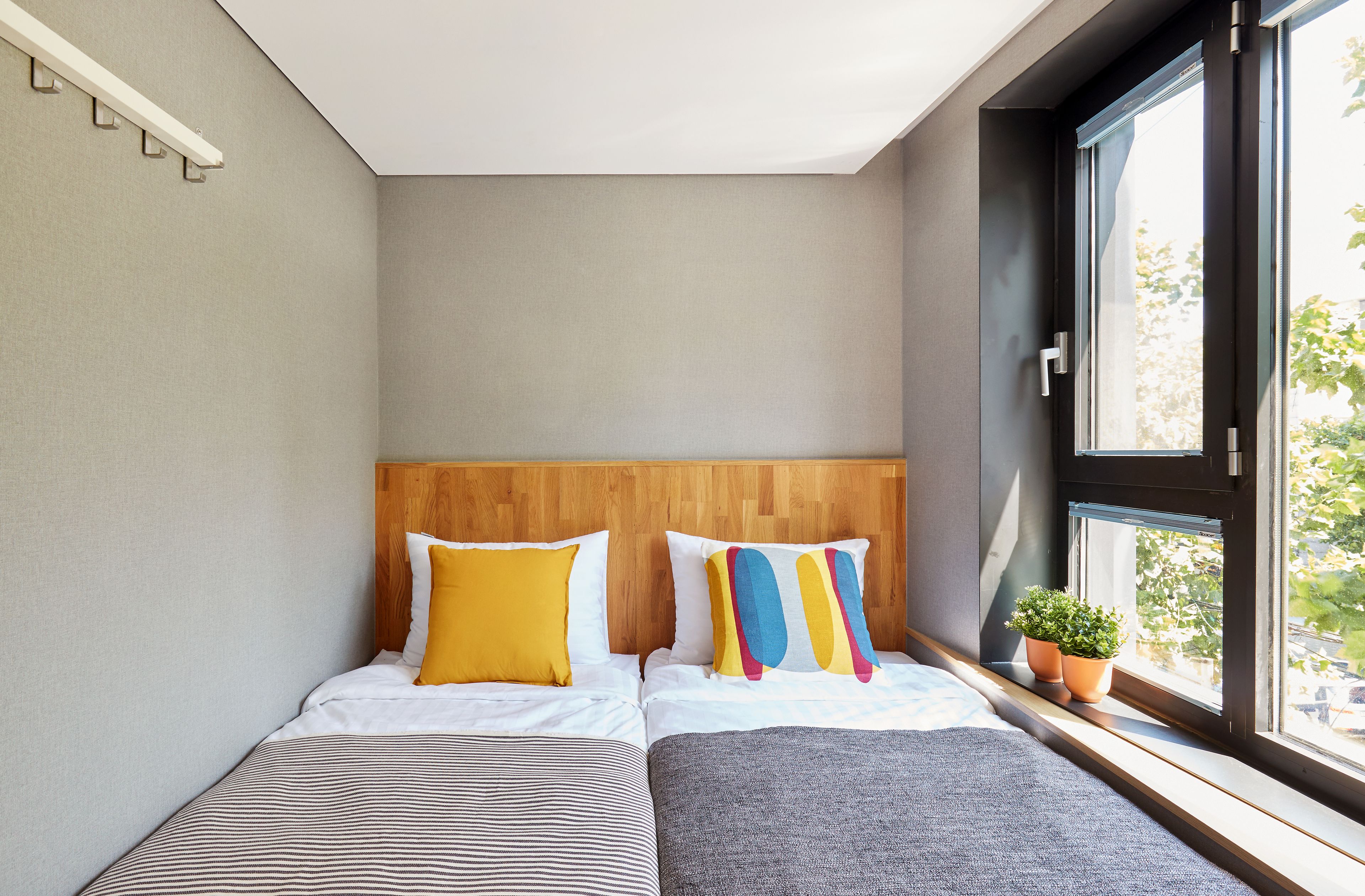 Ein Schlafzimmer mit einem Bett, zwei Kissen, einem Nachttisch mit Pflanze und einem Fenster mit Blick.