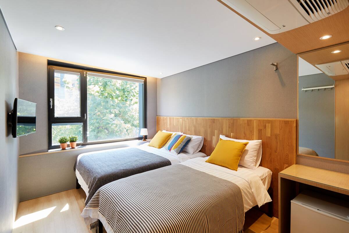A modern hotel room with two beds, a large window, and a small desk.