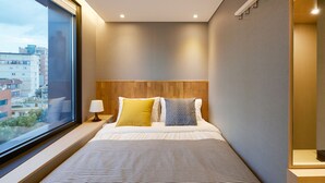 A modern hotel room with a large window, a wooden headboard, and a striped bedspread.