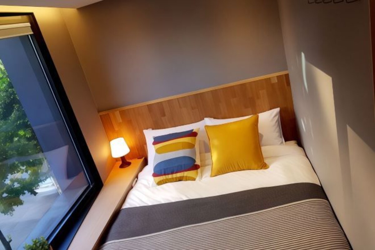 A hotel room with a large window, a wooden headboard, and a bed with striped bedding and colorful pillows.