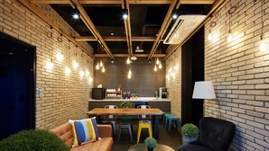 A modern interior with exposed brick walls, wooden beams, and a central dining area with colorful stools.