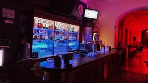 Un bar con mostrador, estantes llenos de botellas y un televisor colgado en la pared.