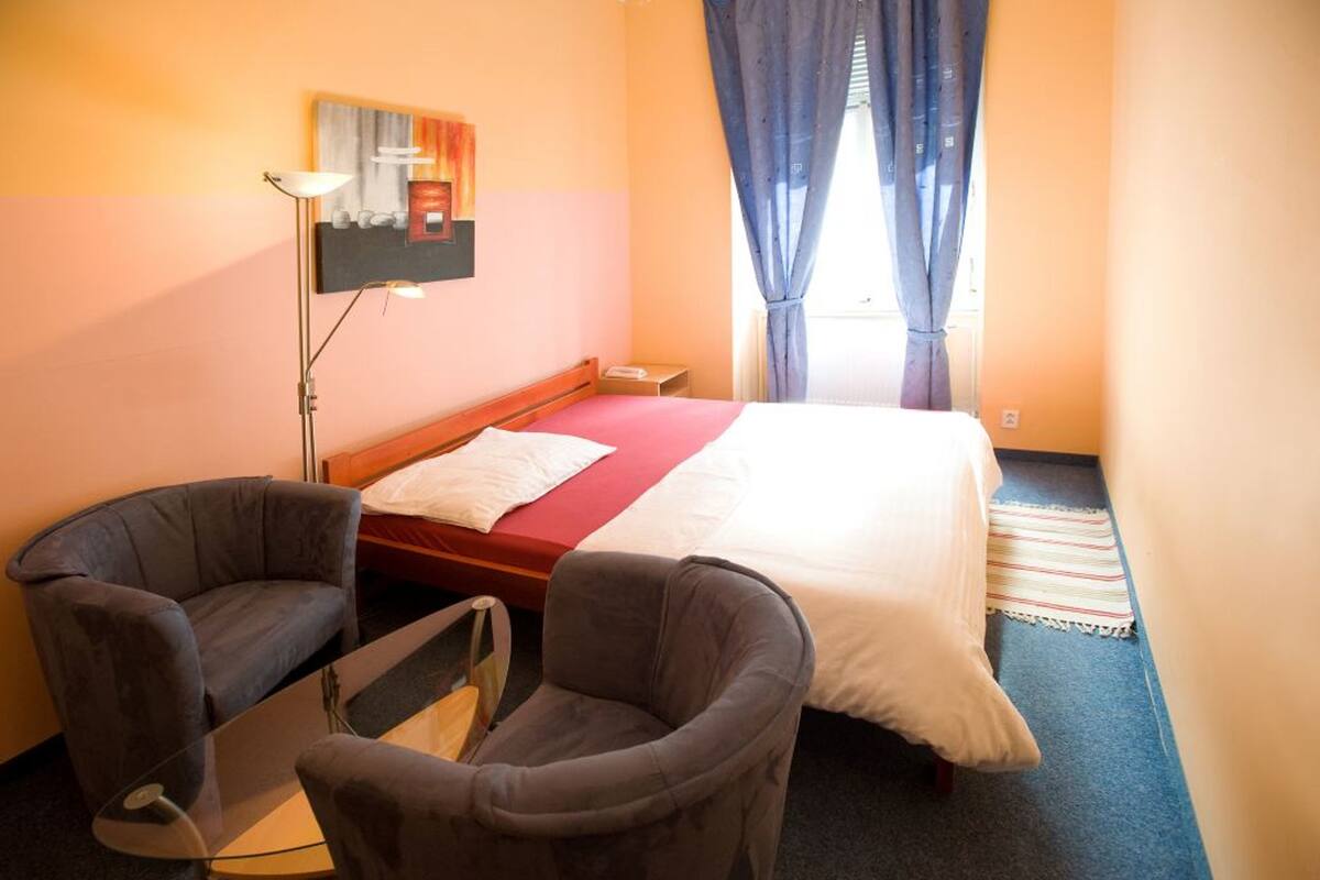 A hotel room with a bed, two armchairs, a desk, a lamp, and a painting on the wall.