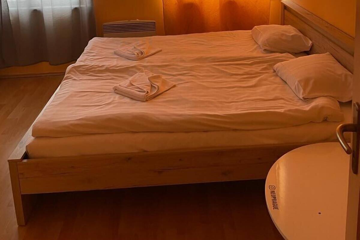 A single bed with white linens and pillows, a wooden headboard, and a white sink to the right.