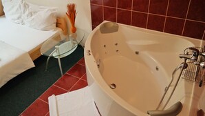 Habitación de hotel con cama, una mesita de cristal con un florero y una bañera con ducha.