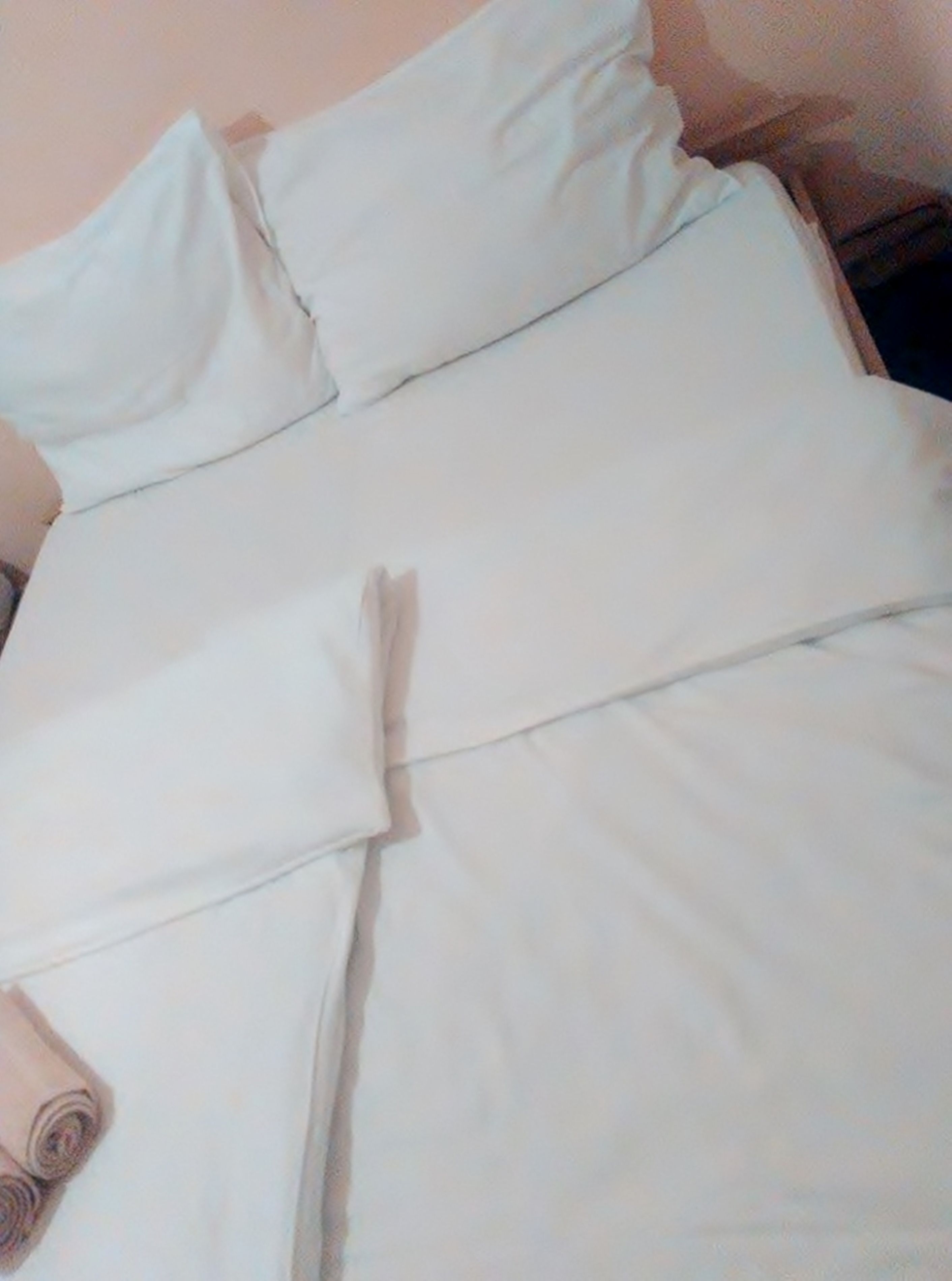 A bed with white bedding and a rolled-up towel on it.