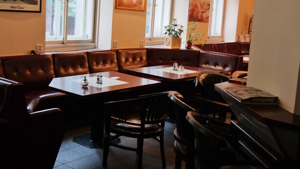 Un restaurante con cabinas, mesas y sillas. Hay ventanas con luz natural y lámparas en la pared.