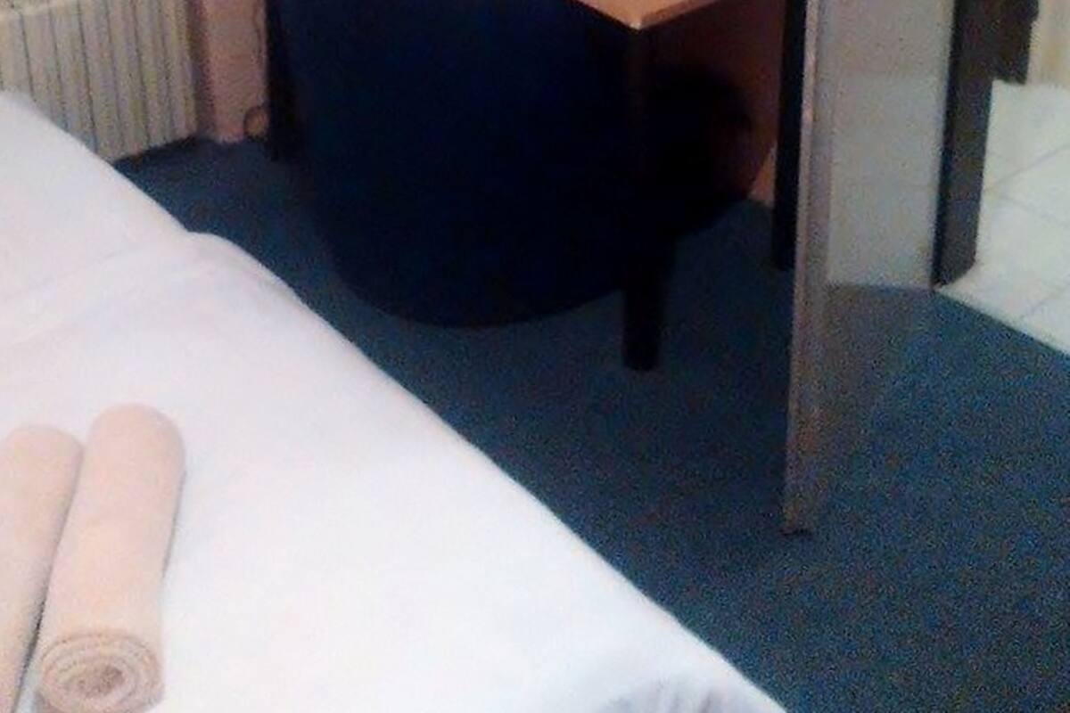 A hotel room with a bed, a desk with a computer and a minibar, and a wardrobe.