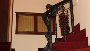 Una escalera con barandillas de metal negro ornamentadas y peldaños cubiertos de alfombra roja.