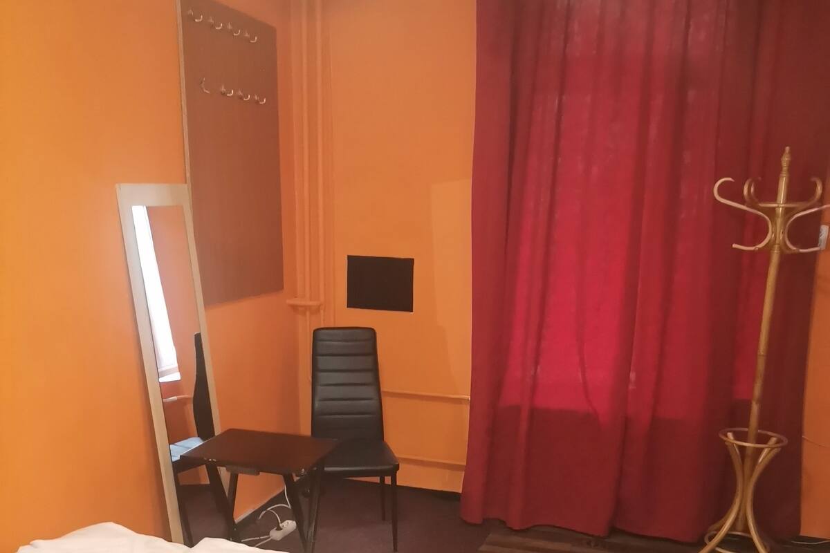 A hotel room with a bed, a desk, a chair, a mirror, and a red curtain.