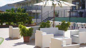 Un espacio de estar al aire libre con mobiliario de mimbre blanco, plantas en macetas y una escalera que lleva a un nivel superior.